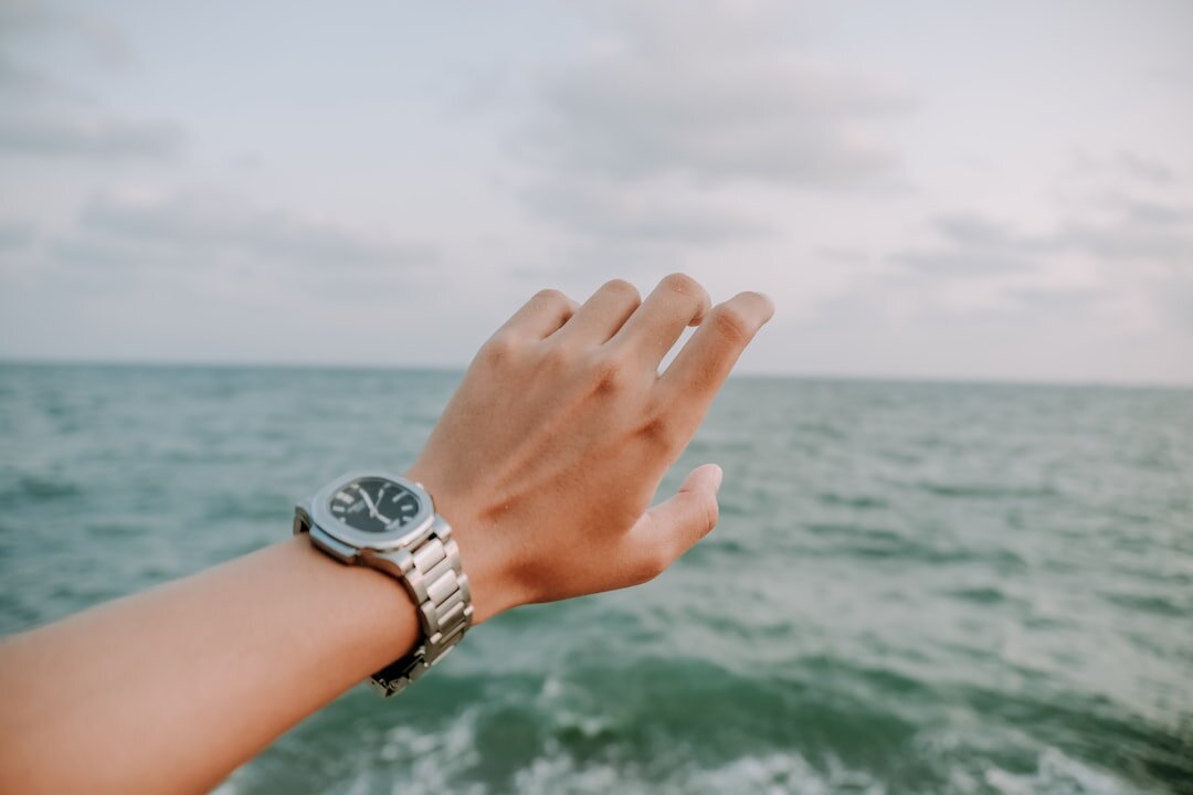 Steel dive watch with blue bezel on a wrist near the ocean